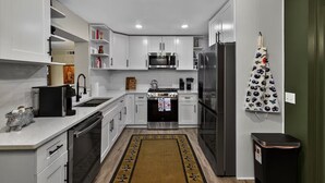 Een moderne keuken met witte kastjes, roestvrijstalen apparatuur en een zwarte prullenbak.