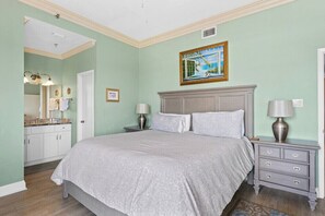 A bedroom with a large bed, a nightstand with a lamp, a dresser, and a bathroom visible in the background. - Phoenix III 3159: Beach Access (Orange Beach)