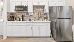 Una cocina moderna con armarios blancos, un refrigerador de acero inoxidable, un microondas y un lavamanos con salpicadero de piedra.
