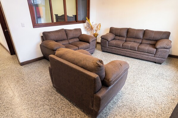 Una sala de estar con dos sofás marrones, una mesita y un florero con plantas secas.