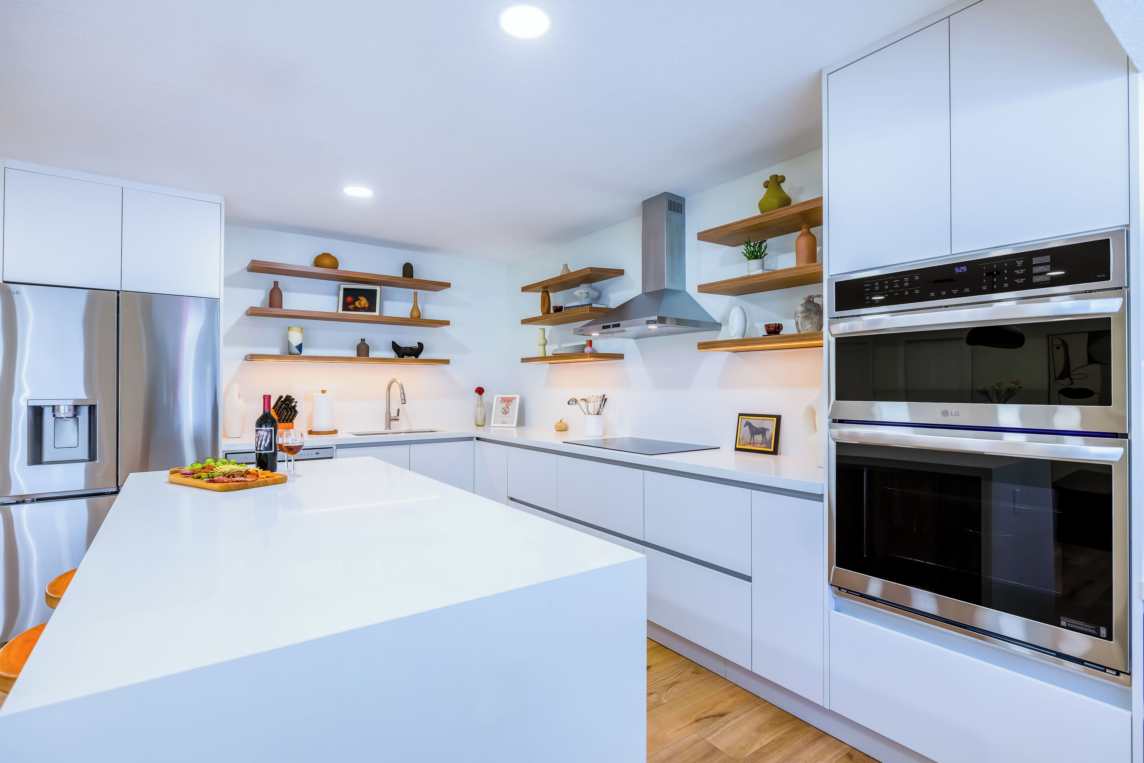 A modern kitchen with white cabinetry, stainless steel appliances, and wooden shelves.