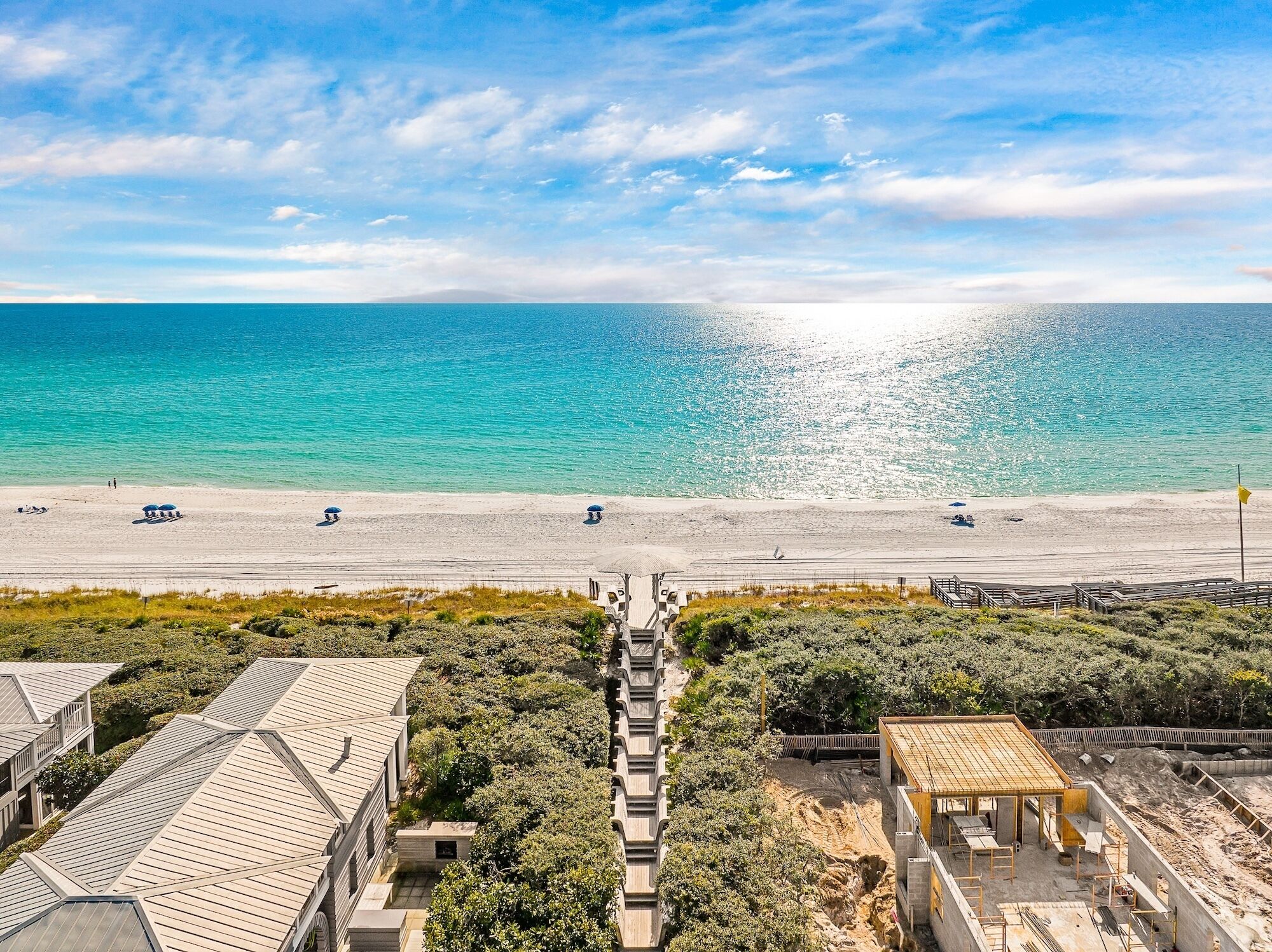 A beach with a clear view of the ocean and a sandy shore. There are buildings with a modern design, some with sloped roofs.