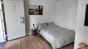 Une chambre à coucher avec un lit, une table de chevet, un tableau accroché au mur et une porte.