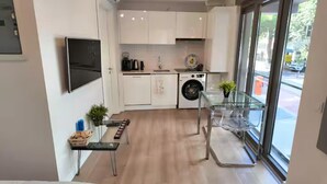 Une cuisine moderne avec des meubles blancs, un lave-linge encastré et une table à manger en verre.
