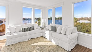 A spacious living room with a large sectional sofa, a patterned rug, and a view of a lake and houses through large windows. - Lakefront with Pool and Gulf Views (Santa Rosa Beach)