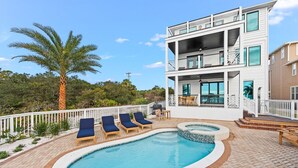 A two-story building with a swimming pool, lounge chairs, and a palm tree. - Lakefront with Pool and Gulf Views (Santa Rosa Beach)