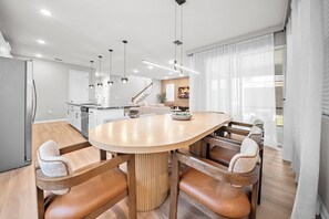 Eine moderne Küche mit einer zentralen Kochinsel, einem Holzesstisch mit gepolsterten Stühlen, Pendelleuchten und einer Treppe zu einer oberen Ebene.