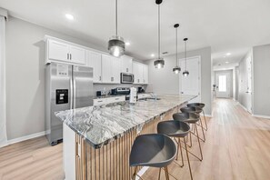 Une cuisine moderne dotée d’un plan de travail en marbre, d’appareils électroménagers en acier inoxydable et de tabourets de bar.