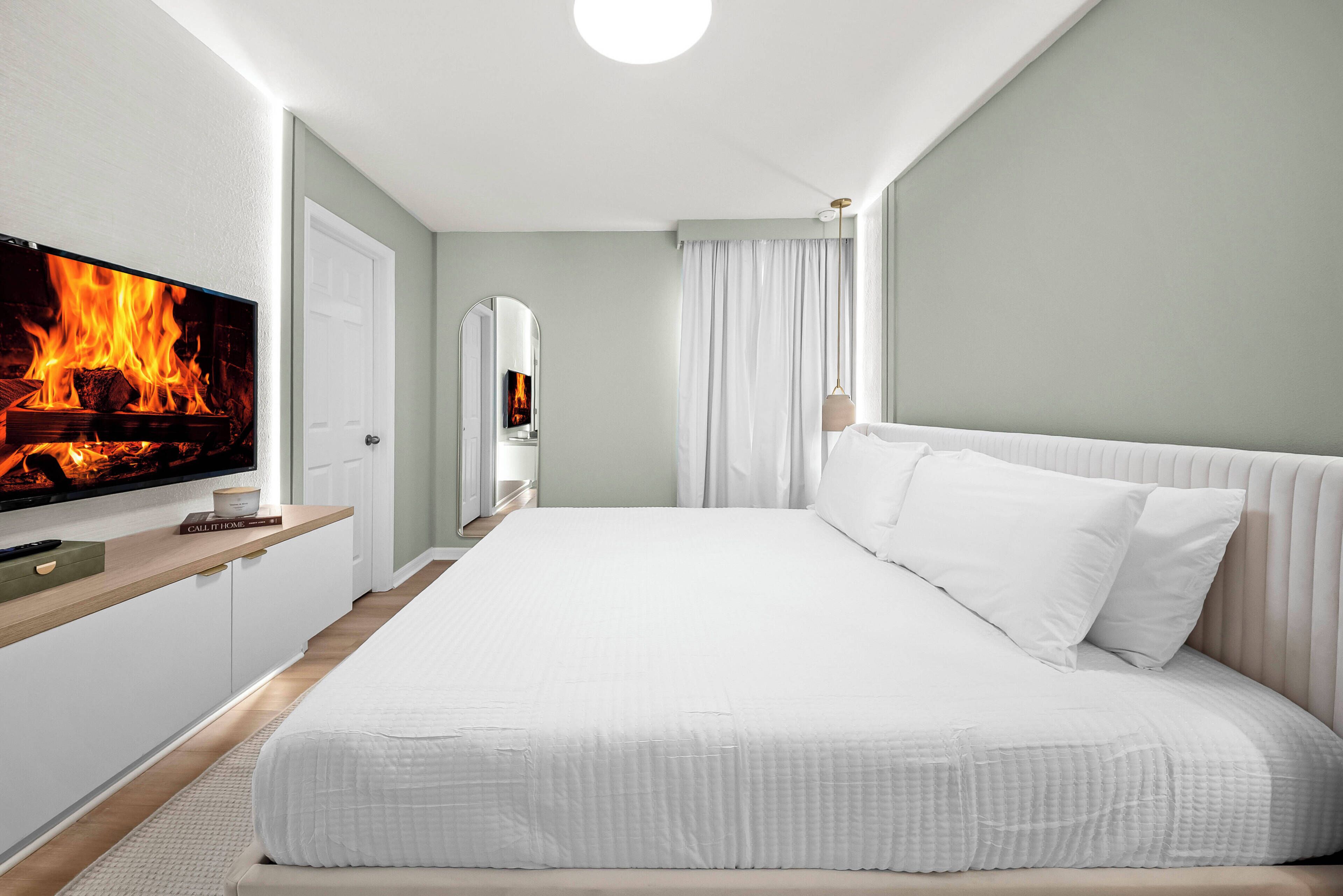Habitación de hotel con una cama grande, un televisor de pantalla plana montado en la pared y una chimenea con llamas visibles.