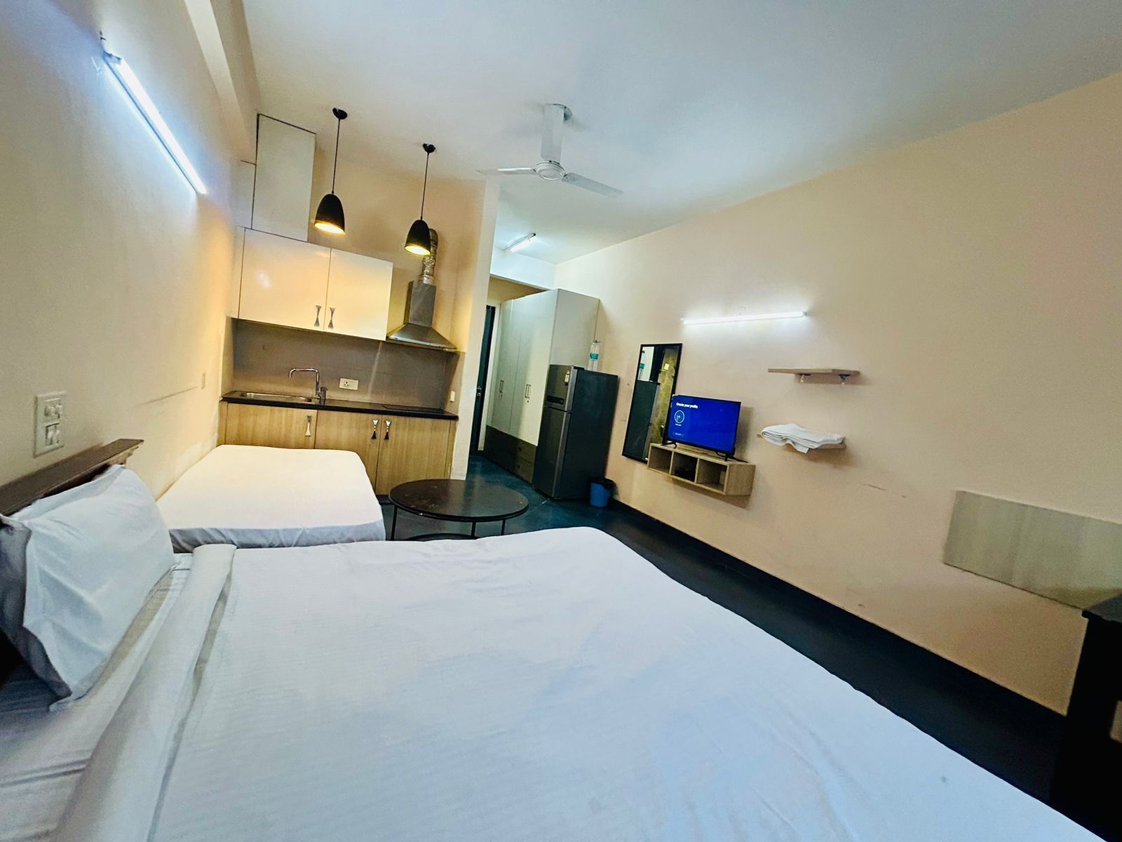 Une chambre d’hôtel avec deux lits, une kitchenette, une télévision et un ventilateur de plafond.