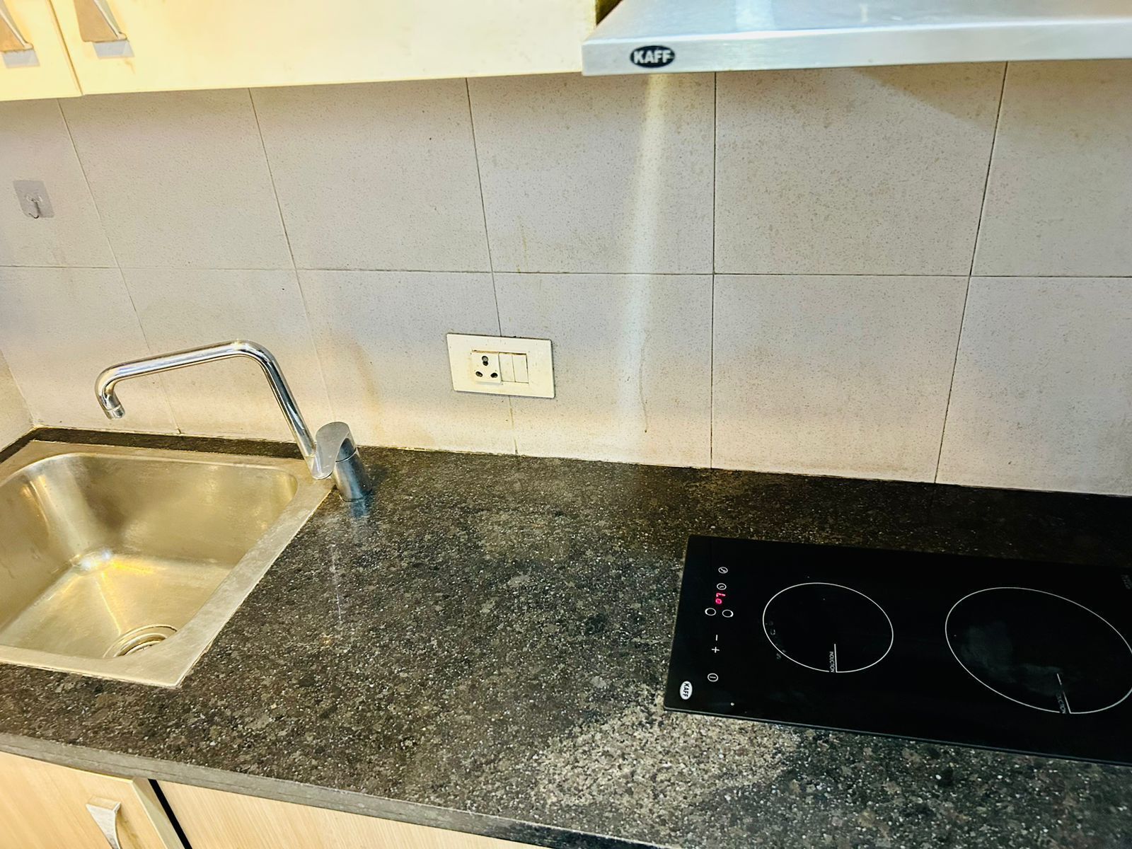 A kitchen with a stainless steel sink, a built-in range hood, and a black induction cooktop.