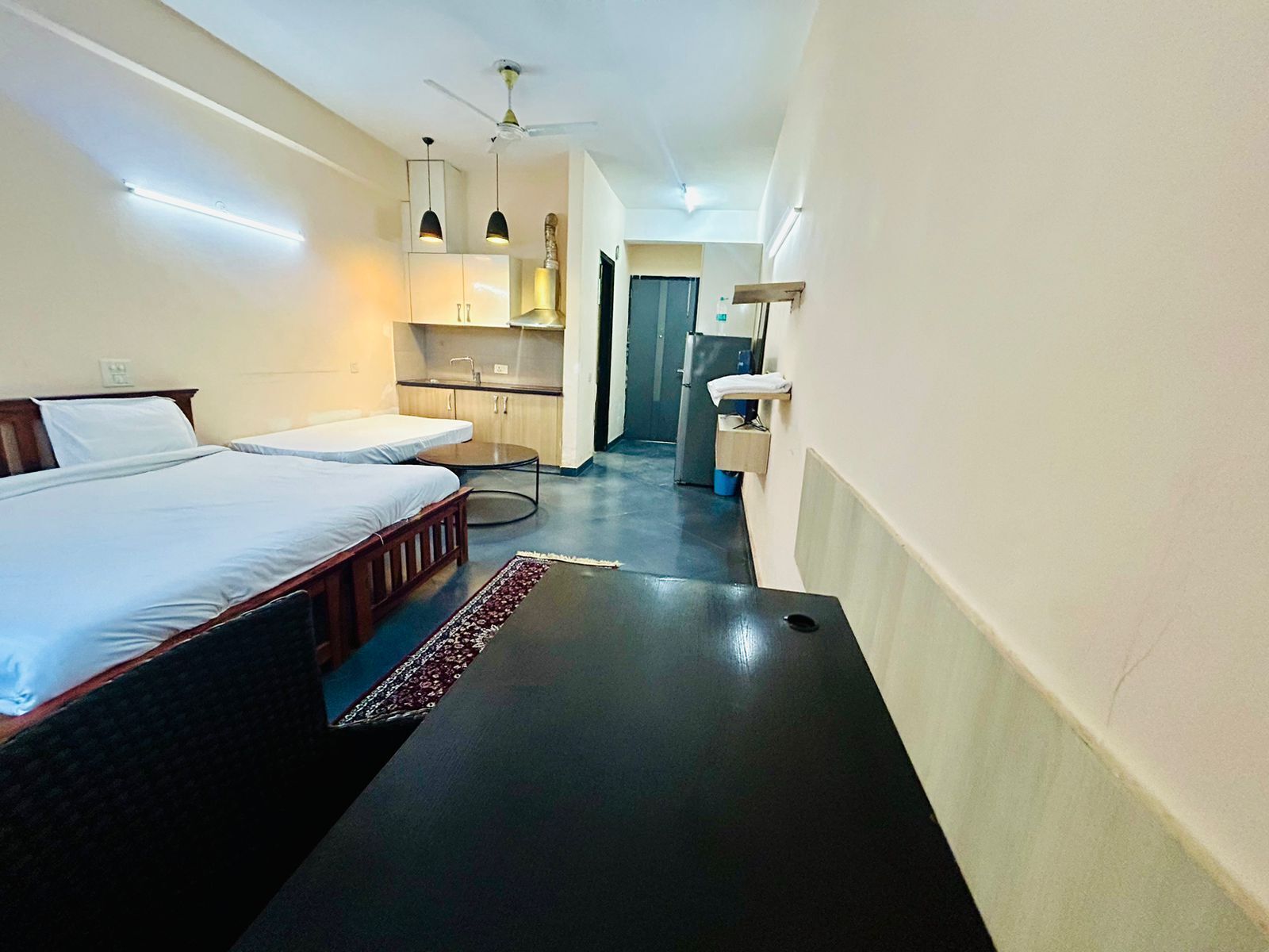A hotel room with a bed, bedside table, and a small kitchenette area.
