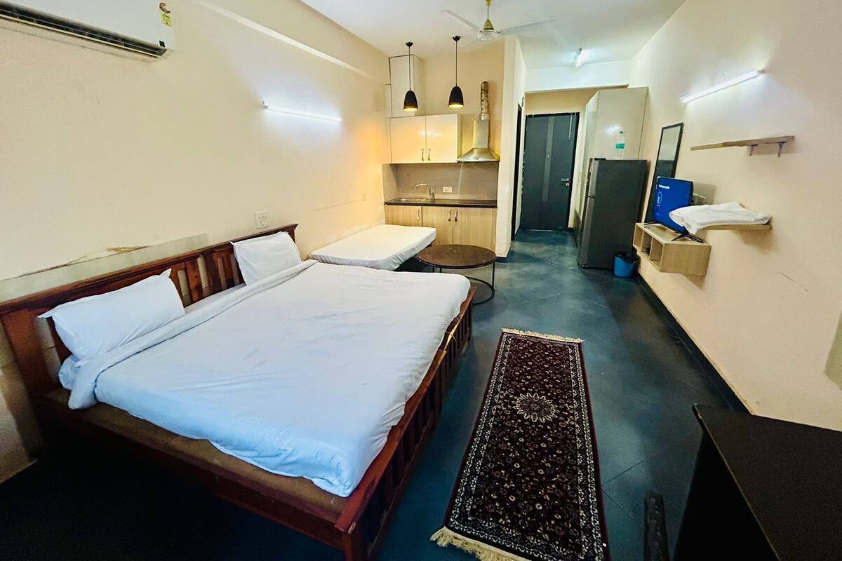 A hotel room with a large bed, a small kitchenette, a desk, and a bathroom.