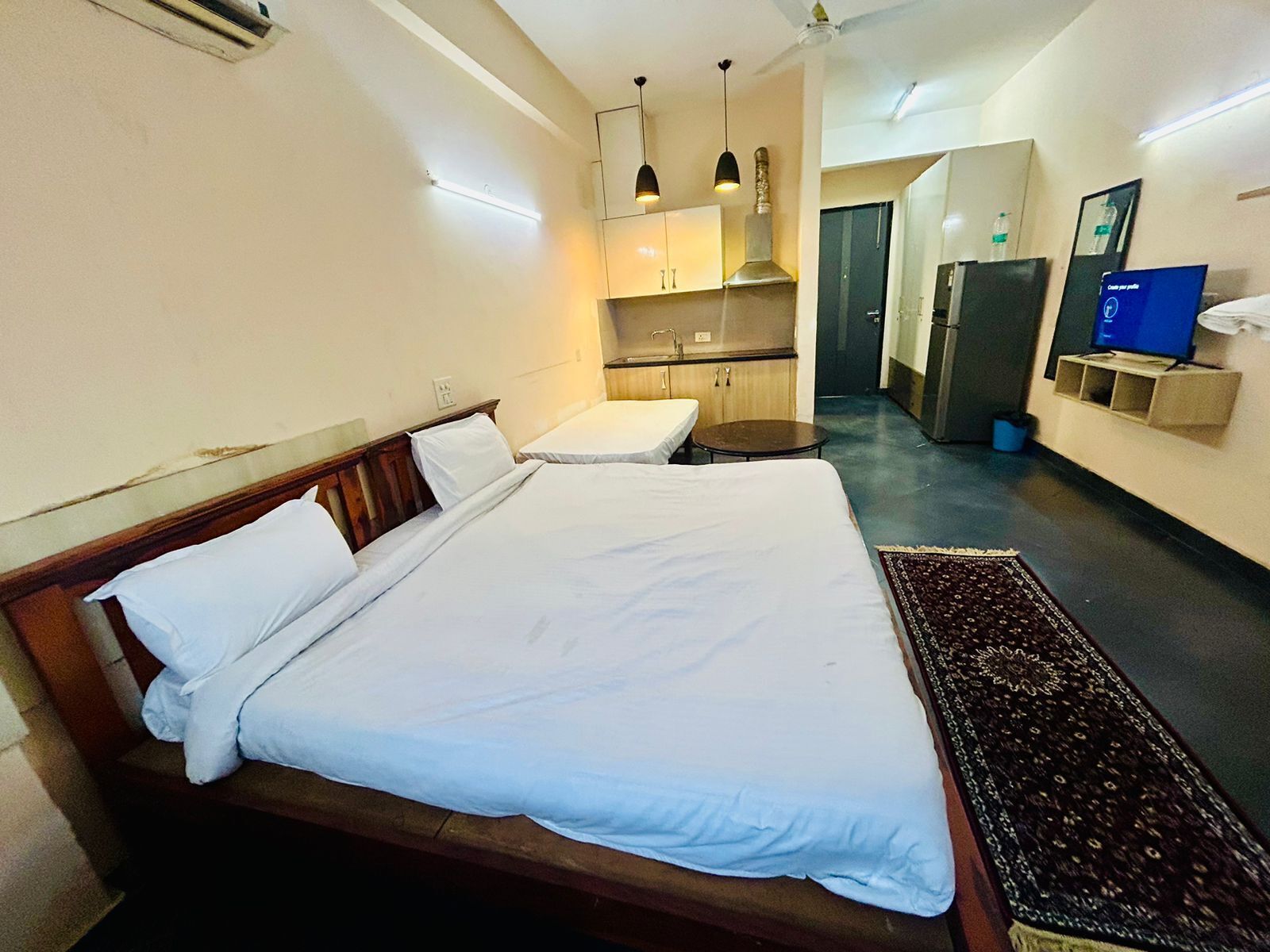 A hotel room with two beds, a kitchenette, a television, and a bathroom.