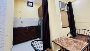 A compact kitchen with a refrigerator, a small window, and a ceiling fan. - Samriddhi Studio Apartment (New Delhi)