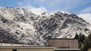Ein Berg mit schneebedeckten Gipfeln und ein modernes Gebäude mit geneigtem Dach im Vordergrund.