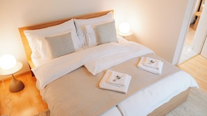 Un lit bien fait, avec des draps blancs, deux oreillers et des serviettes pliées, posés sur une tête de lit en bois.