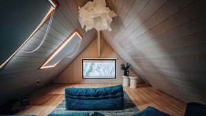 Une pièce mansardée chaleureuse avec un plafond en pente, des murs en bois, une grande fenêtre et un canapé bleu.
