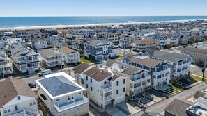 A coastal residential area with multiple-story houses, a beach in the background, and a clear sky. - 4BR/3BA Beach Home w/ Rooftop Deck & Outdoor Living (Ocean City)