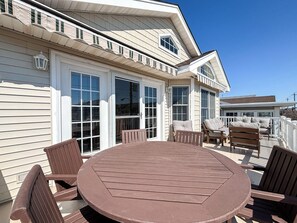 En overdækket terrasse med et rundt bord og træstole, store vinduer og en hvid facade.