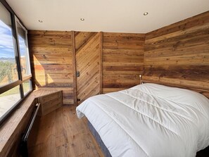 A bedroom with a large bed, wooden walls, a window with a view, and a built-in bench. - 3rd floor, balcony, tv, ski locker, 26m², Vars (Vars)