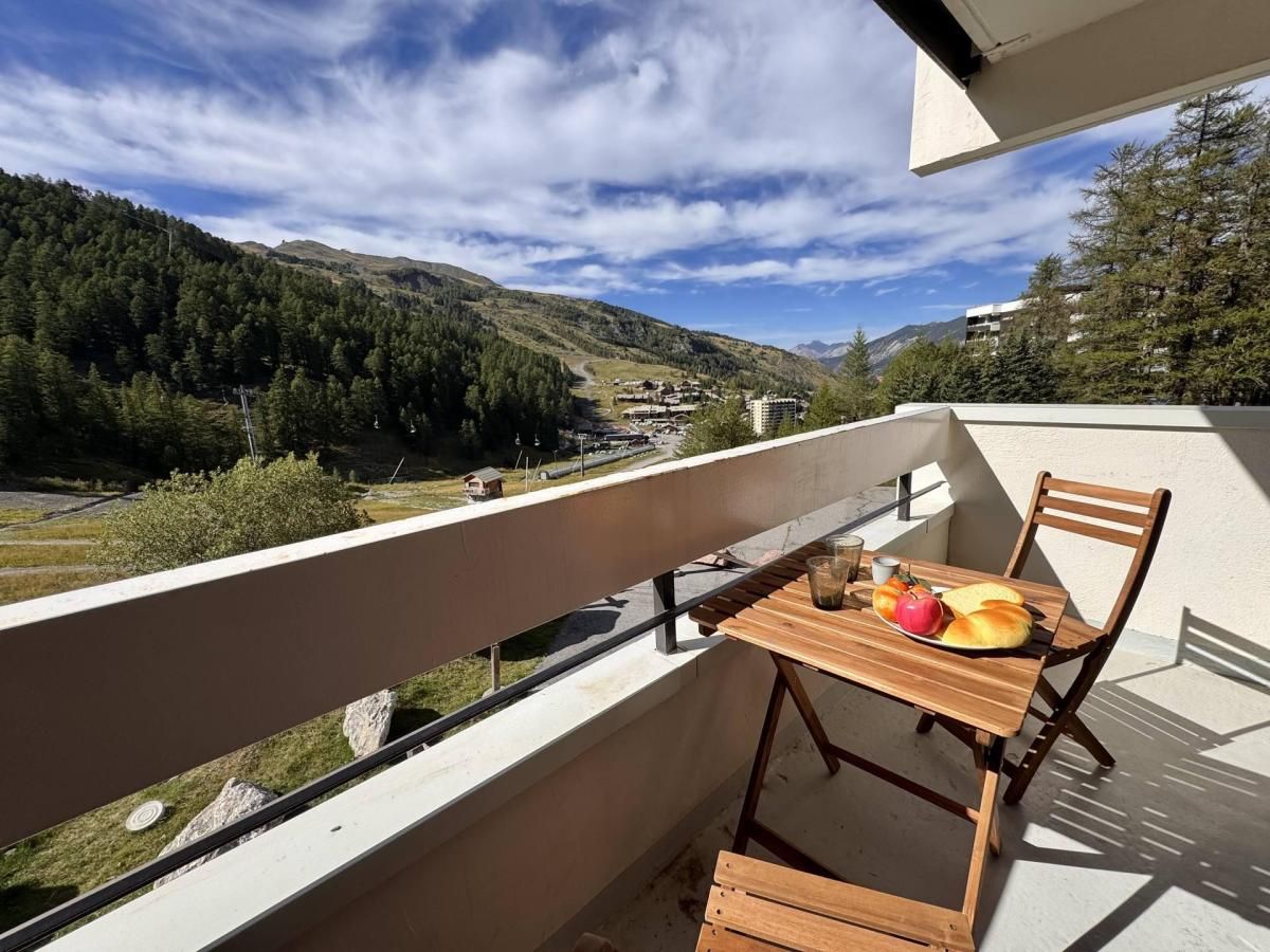 A balcony with a table and chairs, overlooking a mountainous landscape with a clear sky.