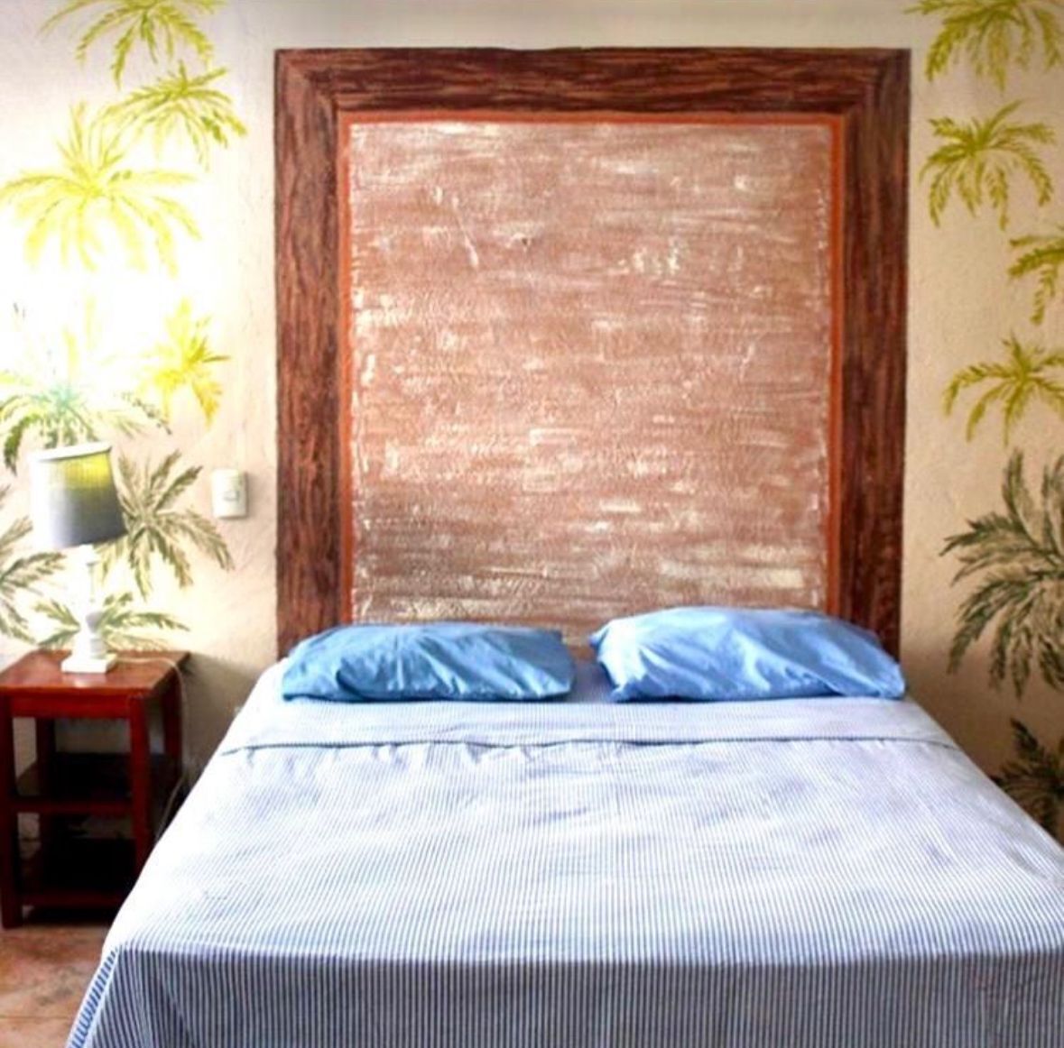 A bed with a striped bedspread and two pillows, a wooden headboard, and a small table with a lamp.