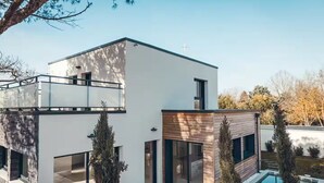 Una casa moderna de dos pisos con techo plano, ventanas amplias y una piscina.