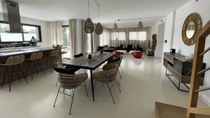 Una cocina moderna con una isla central, comedor con sillas de mimbre y una escalera que sube a un nivel superior.