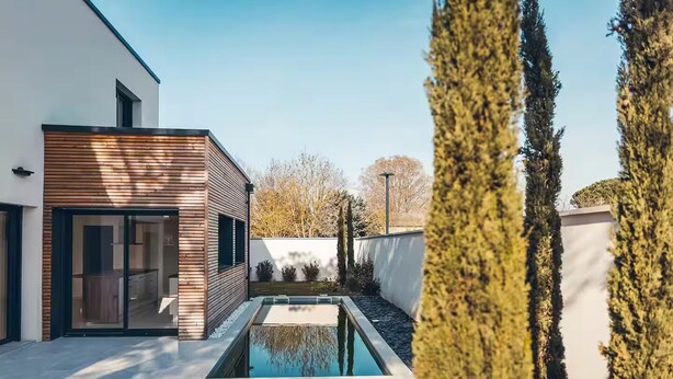 Un edificio moderno con fachada de madera y una piscina rectangular en el centro.