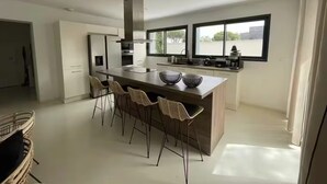 Una cocina moderna con una isla central, taburetes de bar y un amplio ventanal que proporciona luz natural.