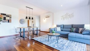 A modern living room with a blue sofa, a dining area with a glass table, and a patterned rug. - Apartamento amplo no Baía da Luz – férias perfeitas para famílias na (Lagos)