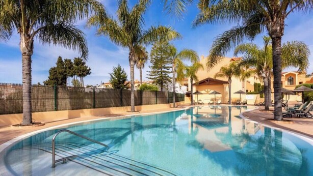 A swimming pool with a curved design, surrounded by palm trees and lounge chairs. - Apartamento amplo no Baía da Luz – férias perfeitas para famílias na (Lagos)