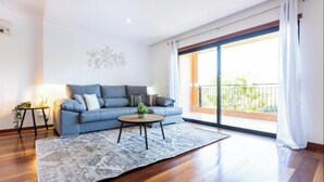 A modern living room with a blue sofa, a round coffee table, and a large window with a balcony. - Apartamento amplo no Baía da Luz – férias perfeitas para famílias na (Lagos)