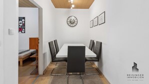 Une salle de conférence avec une table blanche, des chaises noires, un plafond en bois et une horloge au mur.