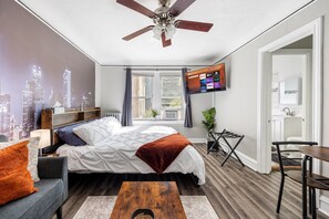 Ein modernes Schlafzimmer mit Stadtbild-Wandgemälde, einem Bett mit weißer und brauner Decke, einem Fernseher an der Wand und einem Holzboden.