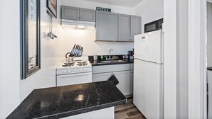 Cocina compacta con armarios blancos, encimera negra, estufa, fregadero y refrigerador.