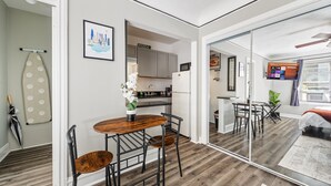 Una cocina moderna con un cartel de pizza, una zona de comedor con una mesa y sillas de madera, y un espejo grande que refleja la habitación.
