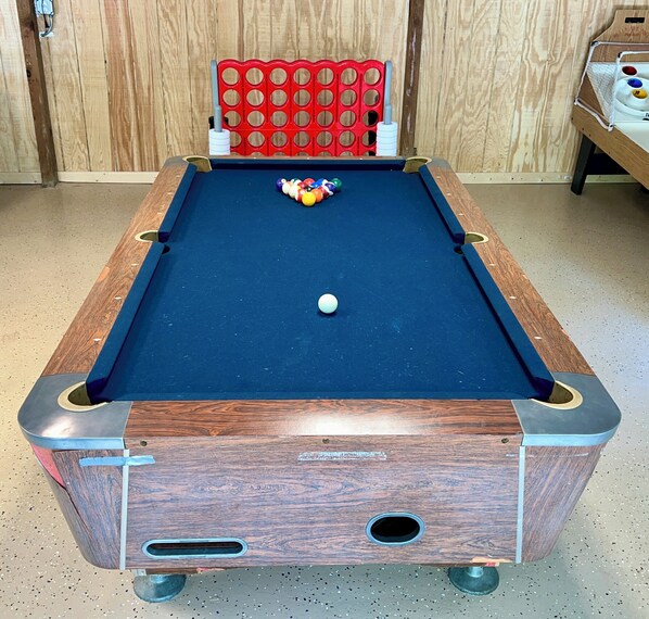 A pool table with a white cue ball, surrounded by colorful balls, in a room with wooden walls and a red chair.
