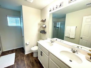 A bathroom with a white sink, two mirrors, a toilet, and a shower. - Suburban Tranquility Meets Metropolitan Convenience (Leander)