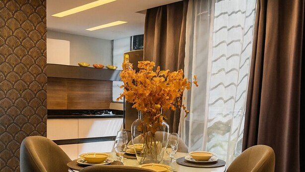 A modern dining area with a round table, four chairs, and a vase of yellow flowers.