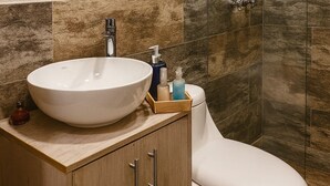 A bathroom with a round mirror, a white sink, a toilet, and a glass shower enclosure.