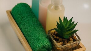 A bathroom sink with three soap dispensers, a green towel, and a small potted plant.