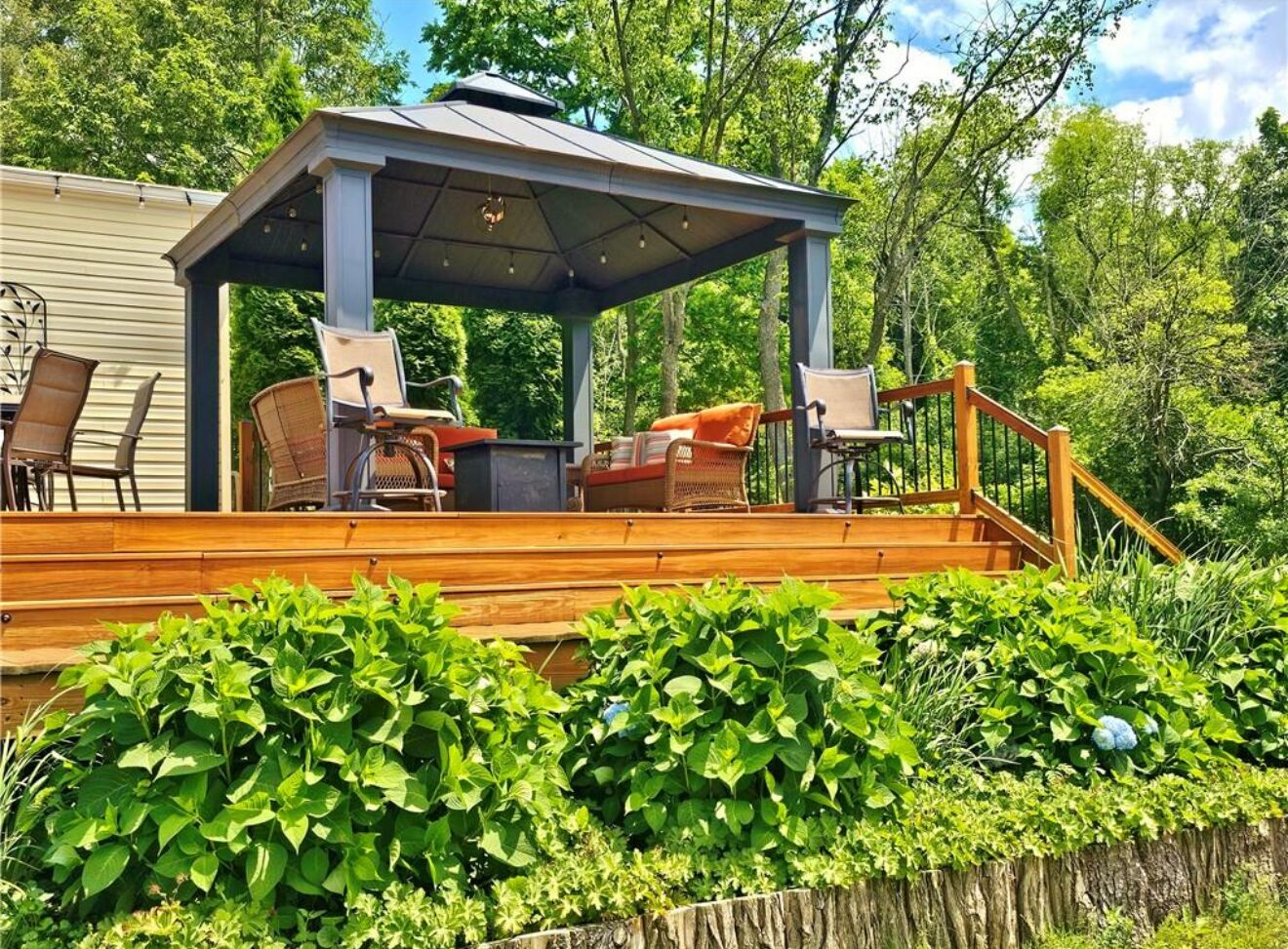 A covered outdoor seating area with a wooden deck, surrounded by lush greenery.