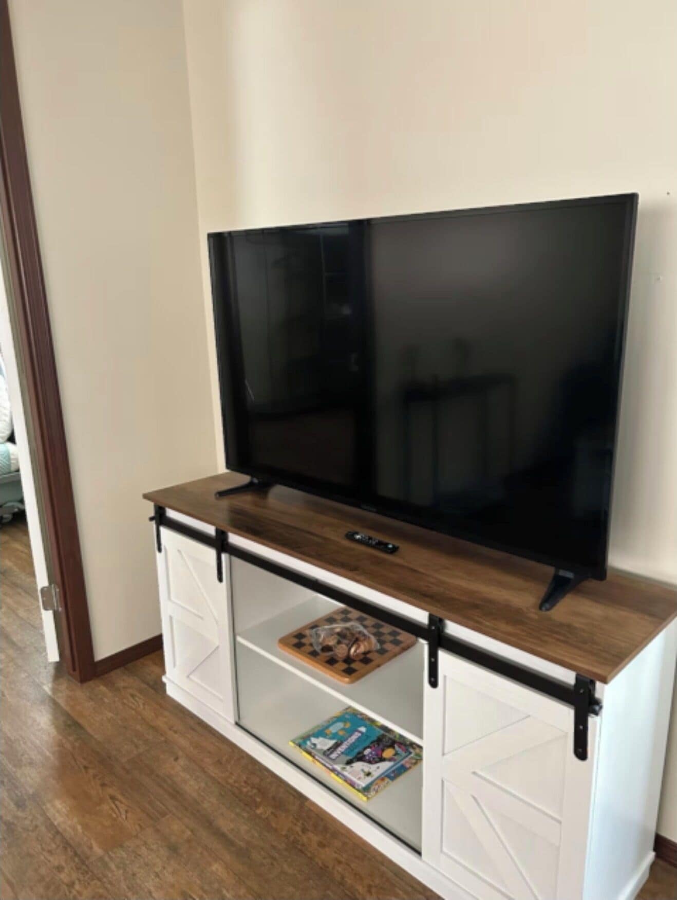 A TV on a wooden cabinet with a glass door, a remote control on the cabinet, and a magazine on the lower shelf.