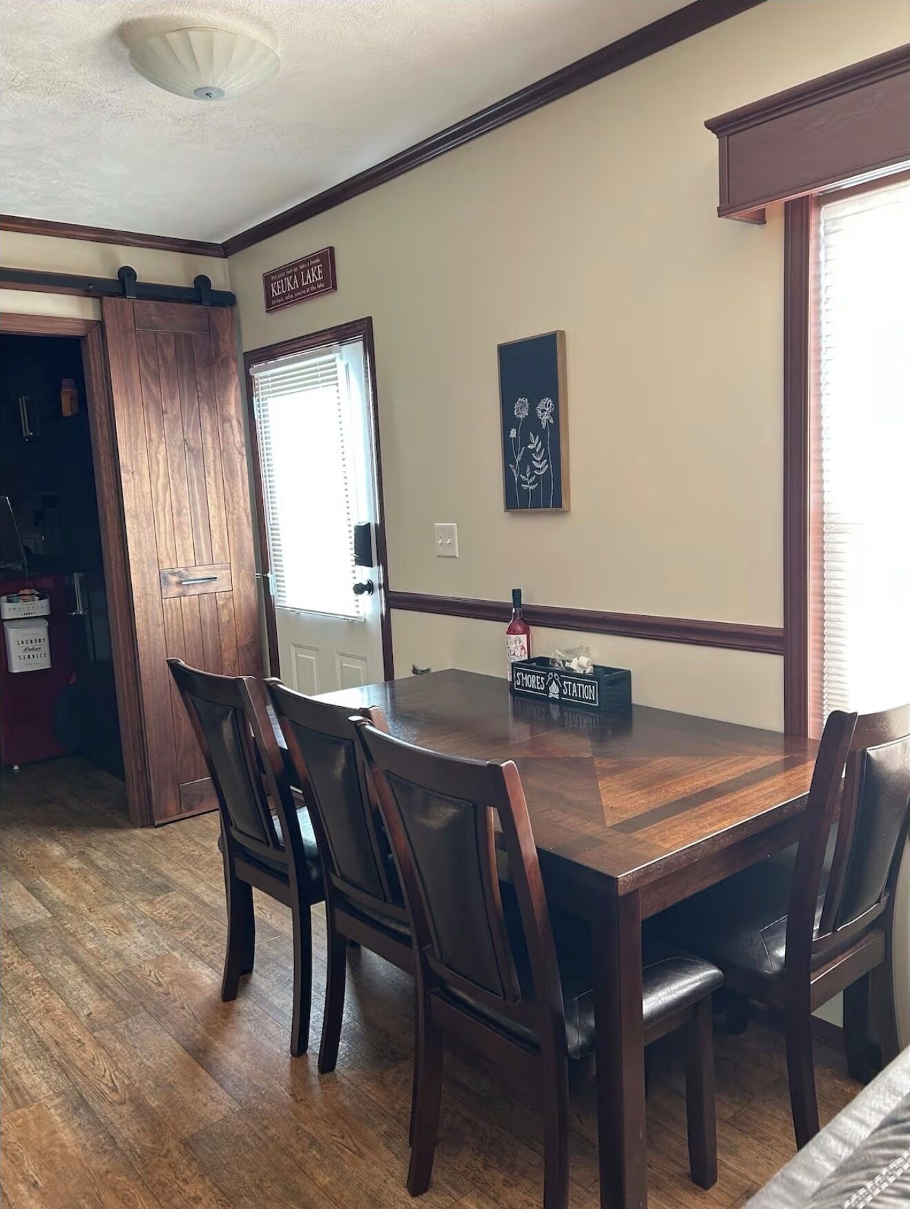 A dining area with a wooden table and chairs, a sign reading "KEUKA LAKE", and a framed picture on the wall.