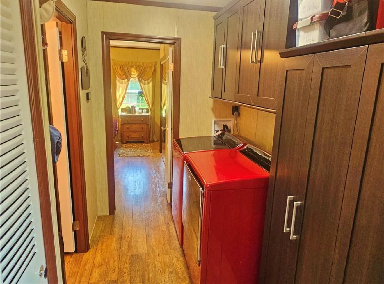 A narrow hallway with wooden flooring, a red appliance, and wooden cabinets.