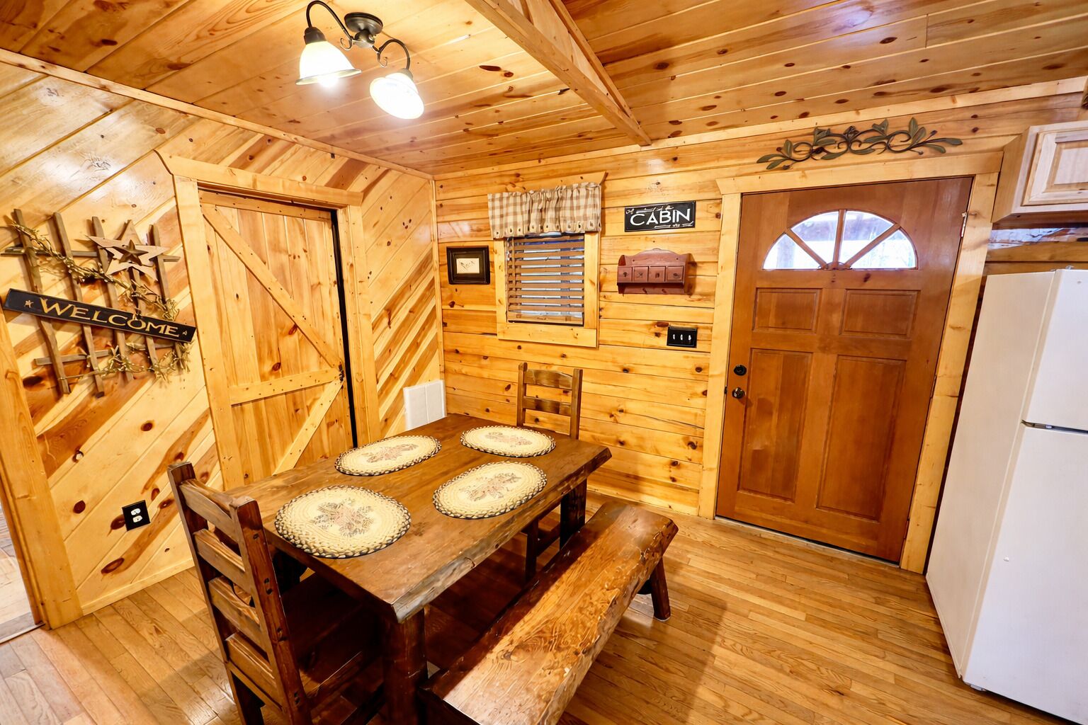 L’intérieur d’un chalet en bois, avec une table à manger, des bancs, un réfrigérateur et une pancarte « Bienvenue ».