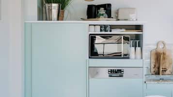 Une cuisine avec un meuble vert turquoise d’époque, un four à micro-ondes, un évier et un coin repas comprenant une table et une chaise blanches.