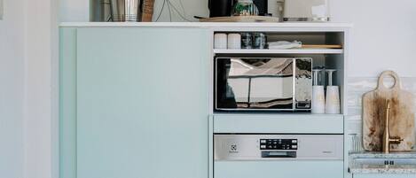 A kitchen with a vintage teal cabinet, a microwave, a sink, and a dining area with a white table and chair.
